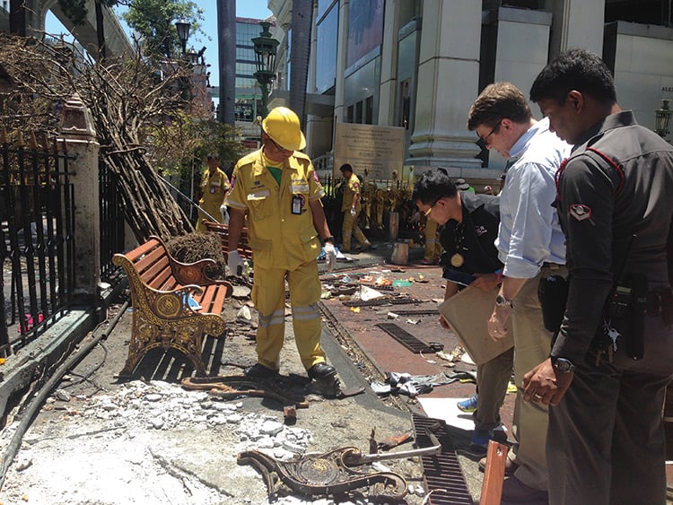 Four men inspecting debris on the ground after the bombing at Erawan Shrine