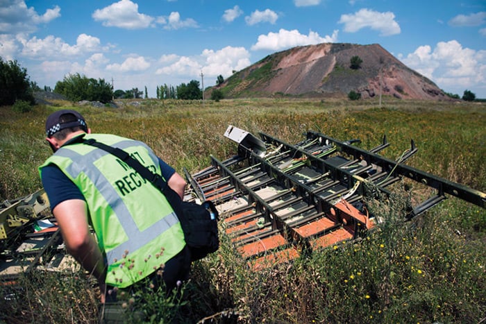 An AFP member inspecting a piece of debris from MH17