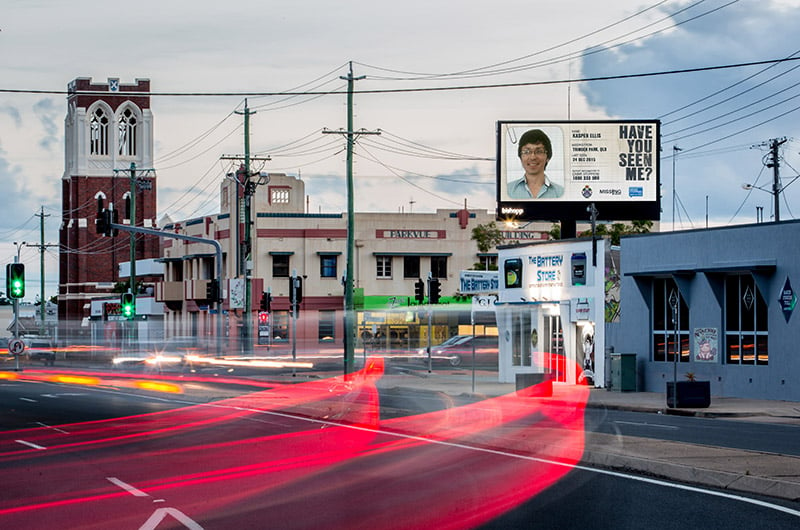 A busy street with a billboard that has a photo of a person on it with the text: Have you seen me?