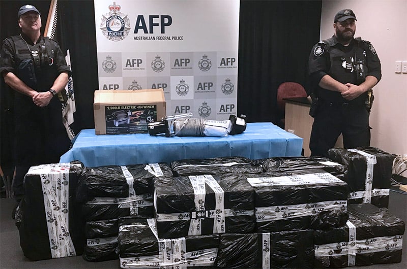 two uniformed officers standing either side of a drug seizure