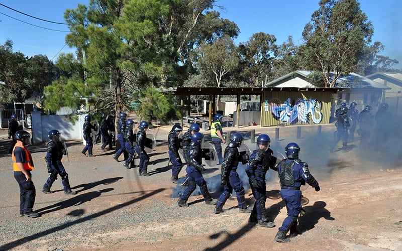 A large number of officers wearing protective helmets and body armour, carrying shields