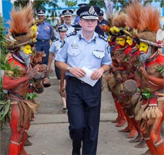 Commissioner Andrew Colvin and other AFP executive officers walking between two lines of people singing and clapping in traditional, colourful native dress in Papua New Guinea. 