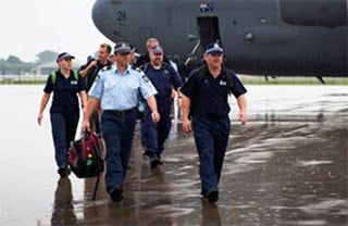 Several uniformed AFP officers on an airport tarmac after exiting a plane.