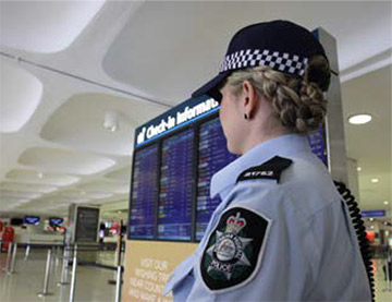 A female AFP officer in front of a check-in information board at an airport.
