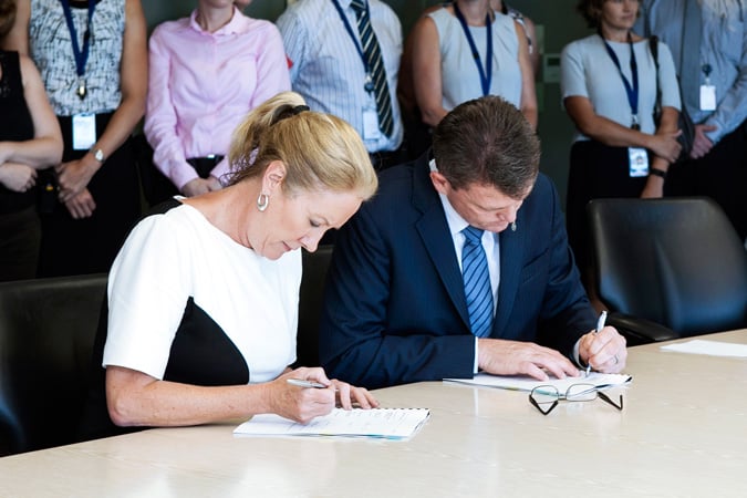 Elizabeth Broderick and AFP Commissioner Andrew Colvin at a desk signing paperwork