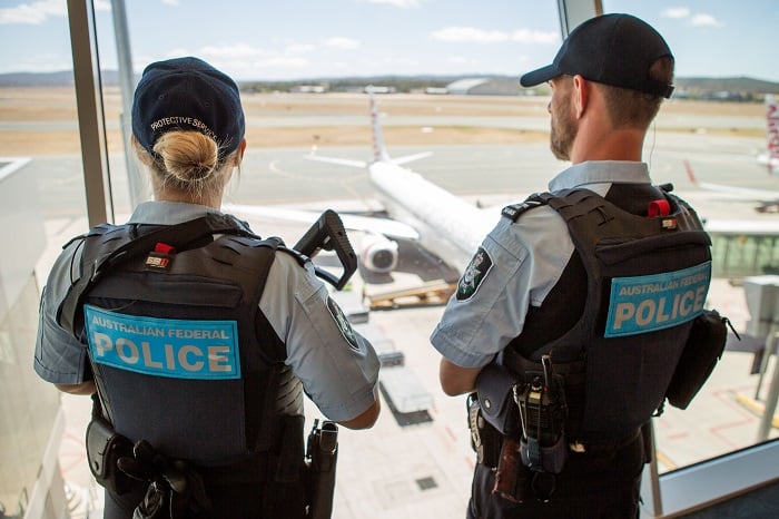 Two AFP Protective Service Officers standing at window at Darwin Aiport overlooking aeroplane on ground