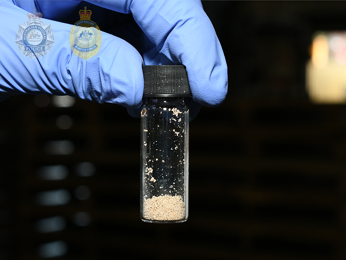 A blue-gloved hand holds a small jar of granulated fentanyl.