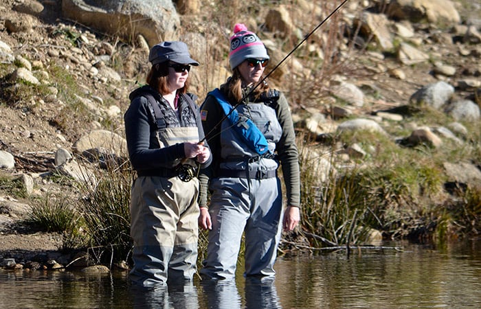two women standing in knee deep water, fly fishing