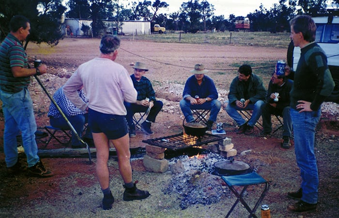 Eight men sitting around a camp fire