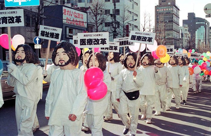 A large group of people dressed in white and wearing masks, marching in a street