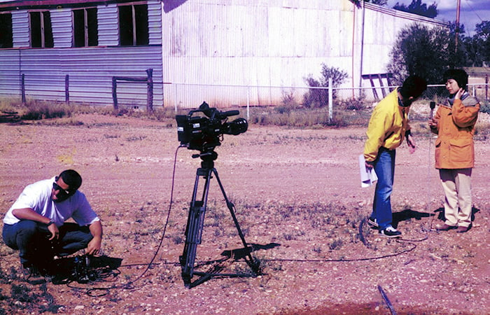 A man setting up a camera with a reporter preparing to speak