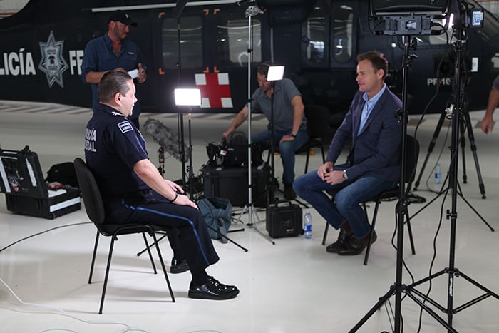 A uniformed officer being interview by a man sitting opposite him