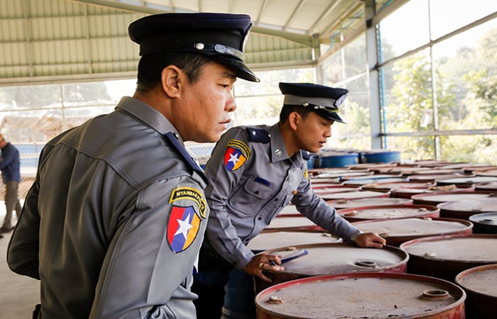 Two uniformed officers inspecting a large number of barrells