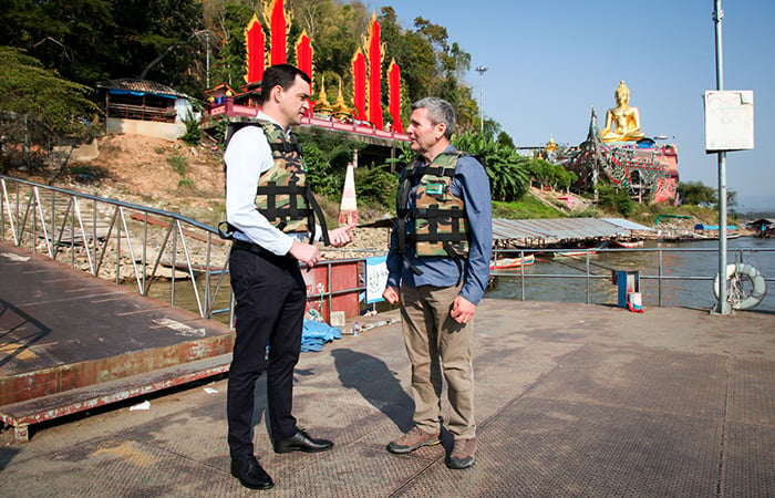 Two men standing on a dock wearing life jackets and talking