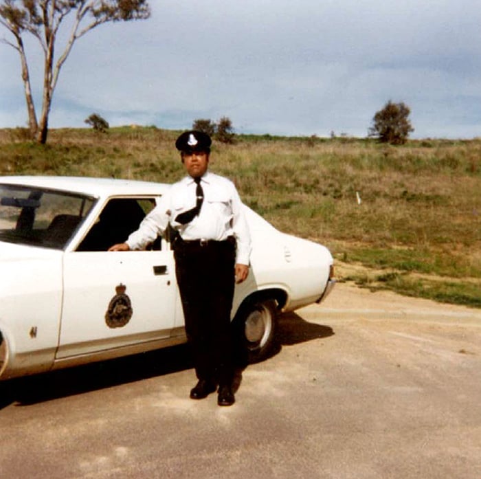 A police officer standing next to a police car many years ago