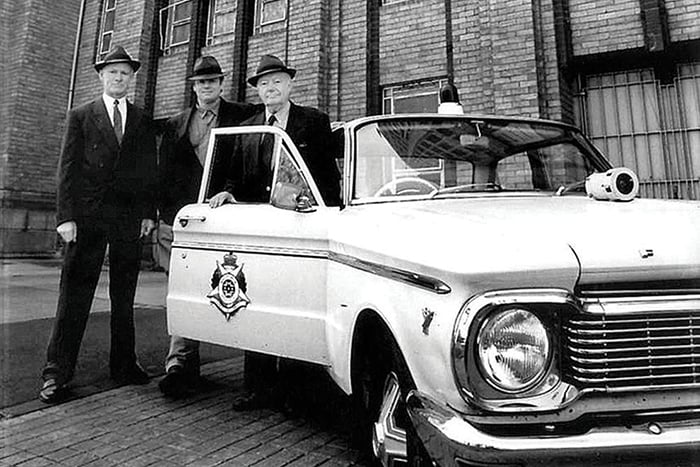 An old photo of three men in suits next to a police car