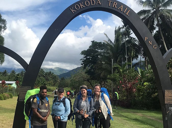 Four people pose for a photo under a sign that reads Kokoda Trail
