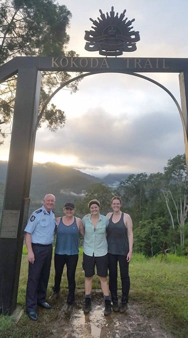 Four people posing for a photo under a sign with the words Kokoda Trail