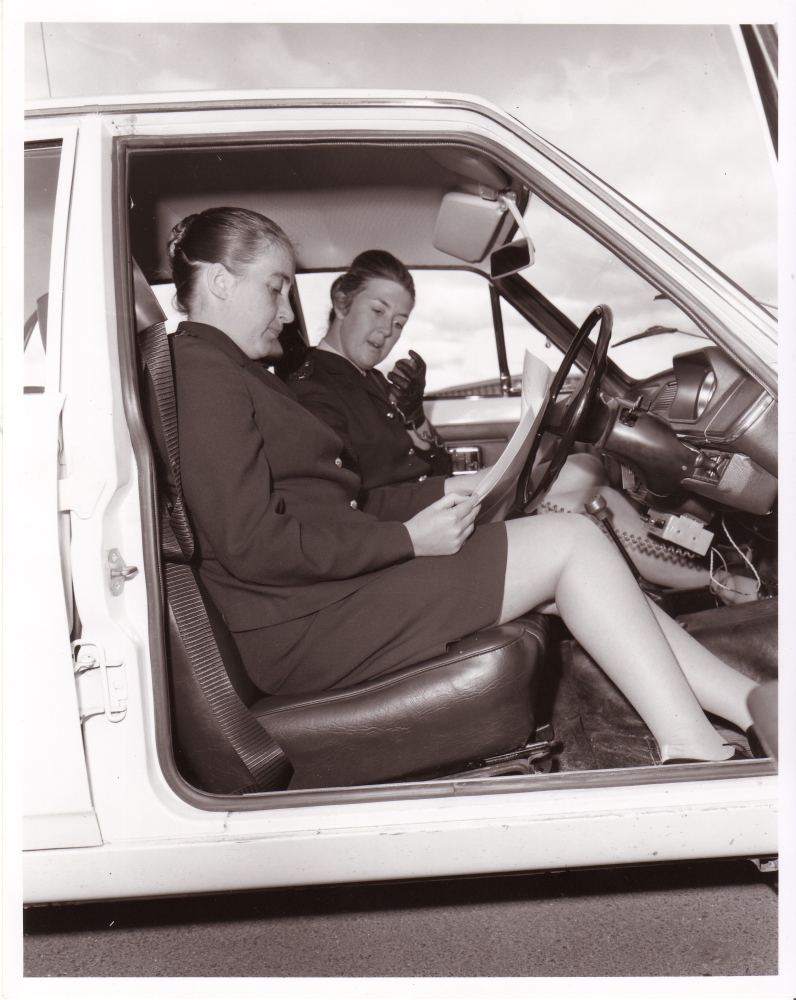Leonie Cavanagh wearing gloves and talking on the radio. Louise Lammin in driver’s seat. Both looking at a sheet of paper in their police car in Canberra in 1972 AFPM426