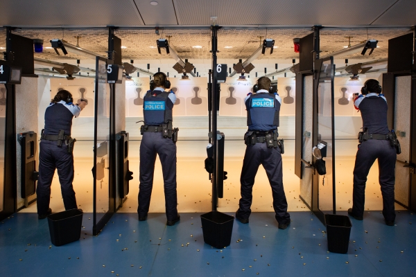 Four police officers in a shooting range training environment pointing guns towards target on a wall