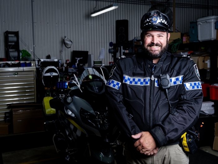 A police officer standing in a garage preparing to ride a police motorbike