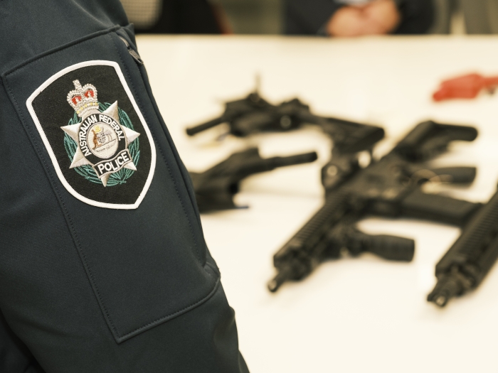 The sleeve of an AFP person standing in front of a table with four large firearms on it