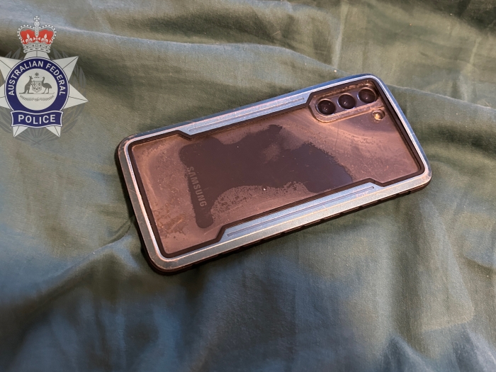 A Samsung phone in a metallic case lies on a green bed sheet