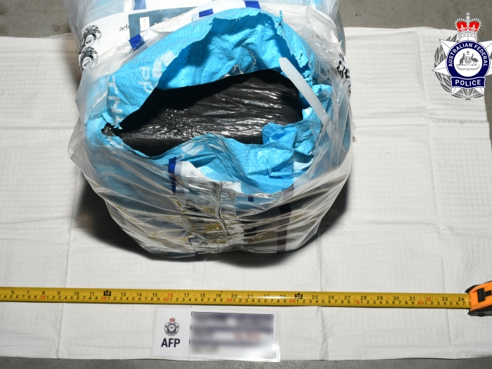 A black-wrapped block of cocaine is concealed within a blue bag.