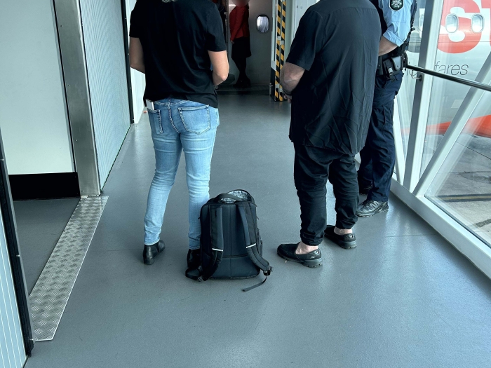 Three people including the POI standing in an airport gangway waiting to enter an aircraft 