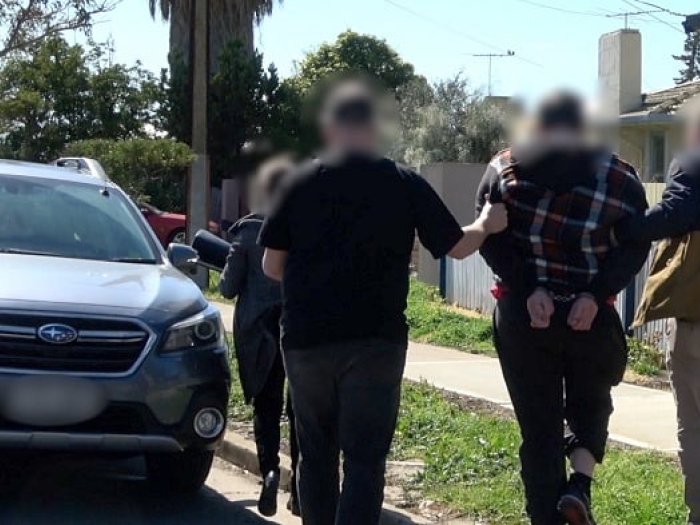 A 19 year old man is led to a vehicle by police following his arrest at a train station