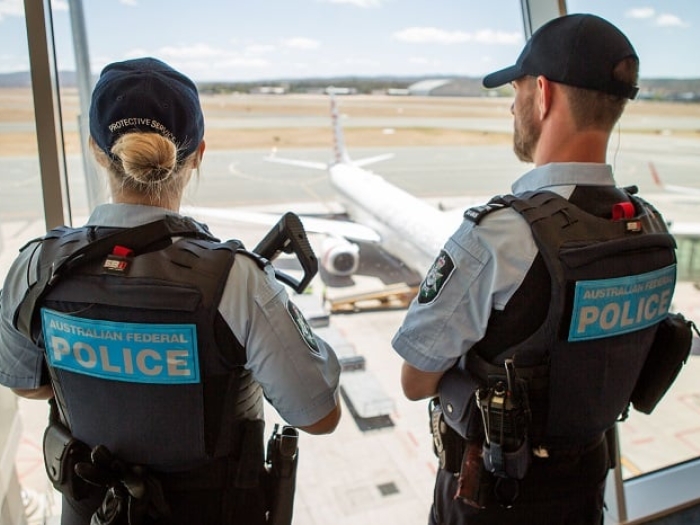 Two AFP Protective Service Officers standing at window at Darwin Aiport overlooking aeroplane on ground