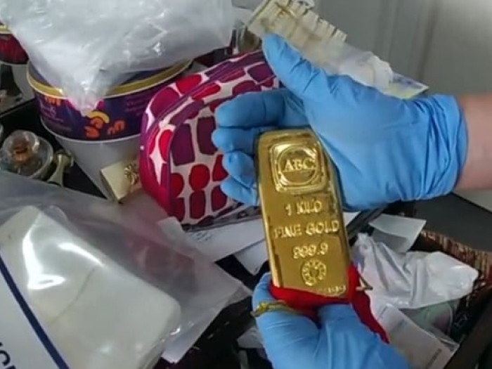 A man wearing blue gloves shows a gold bullion to the camera 