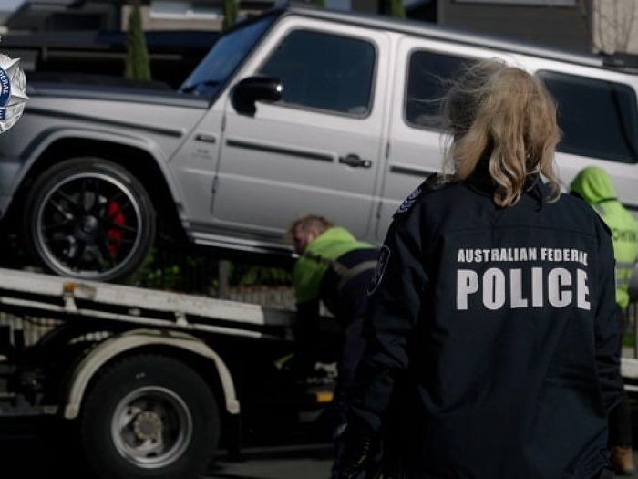 An AFP officer observes a seized silver vehicle being loaded onto a tow truck