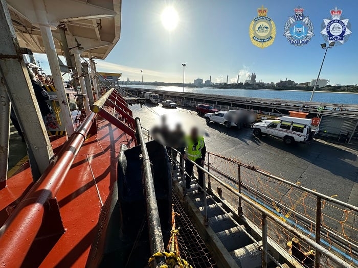 Three people walk up to a bulk carrier docked in WA