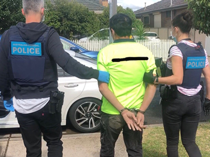 two AFP officers leading handcuffed man in yellow shirt to a car 