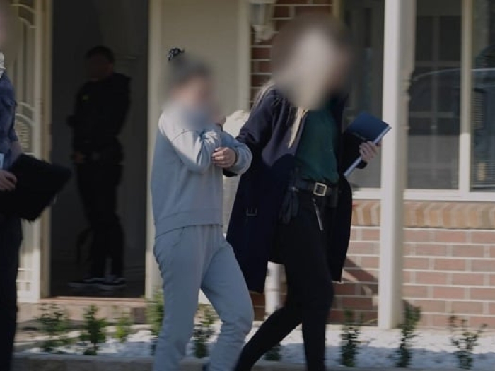 Woman in grey tracksuit being led to a car by AFP officers