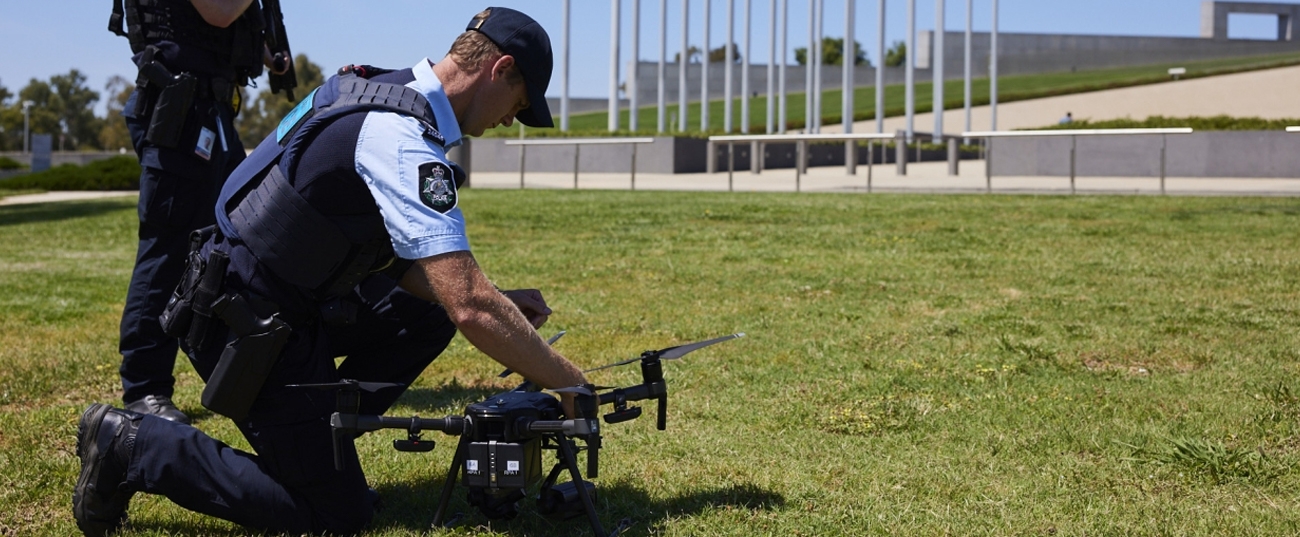 A protective service officer preparing a drone for flight on a lush green lawn