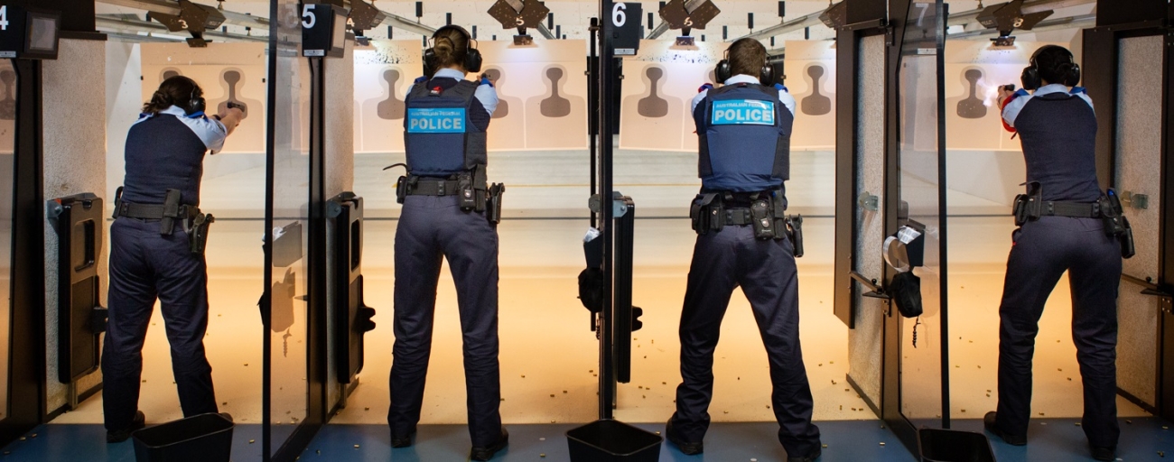 Four police officers in a shooting range training environment pointing guns towards target on a wall